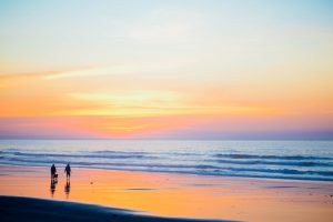 Sunset at the beach and two people walking in the distance practising self care