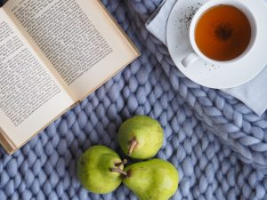 Book laid out beside a cup of tea and some fruit as self care routine