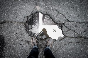 Large pot hole in tarmac in Glasgow with puddle and reflection of man taking a photograph