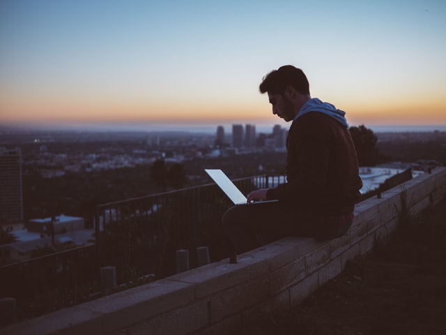 man on laptop sitting on ledge of building